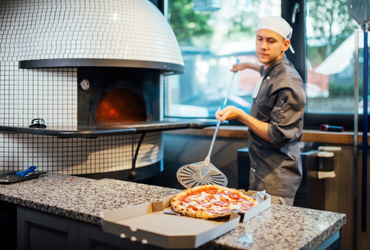 Chef puts freshly baked hot pizza from a spatula in a box. Catering kitchen work.