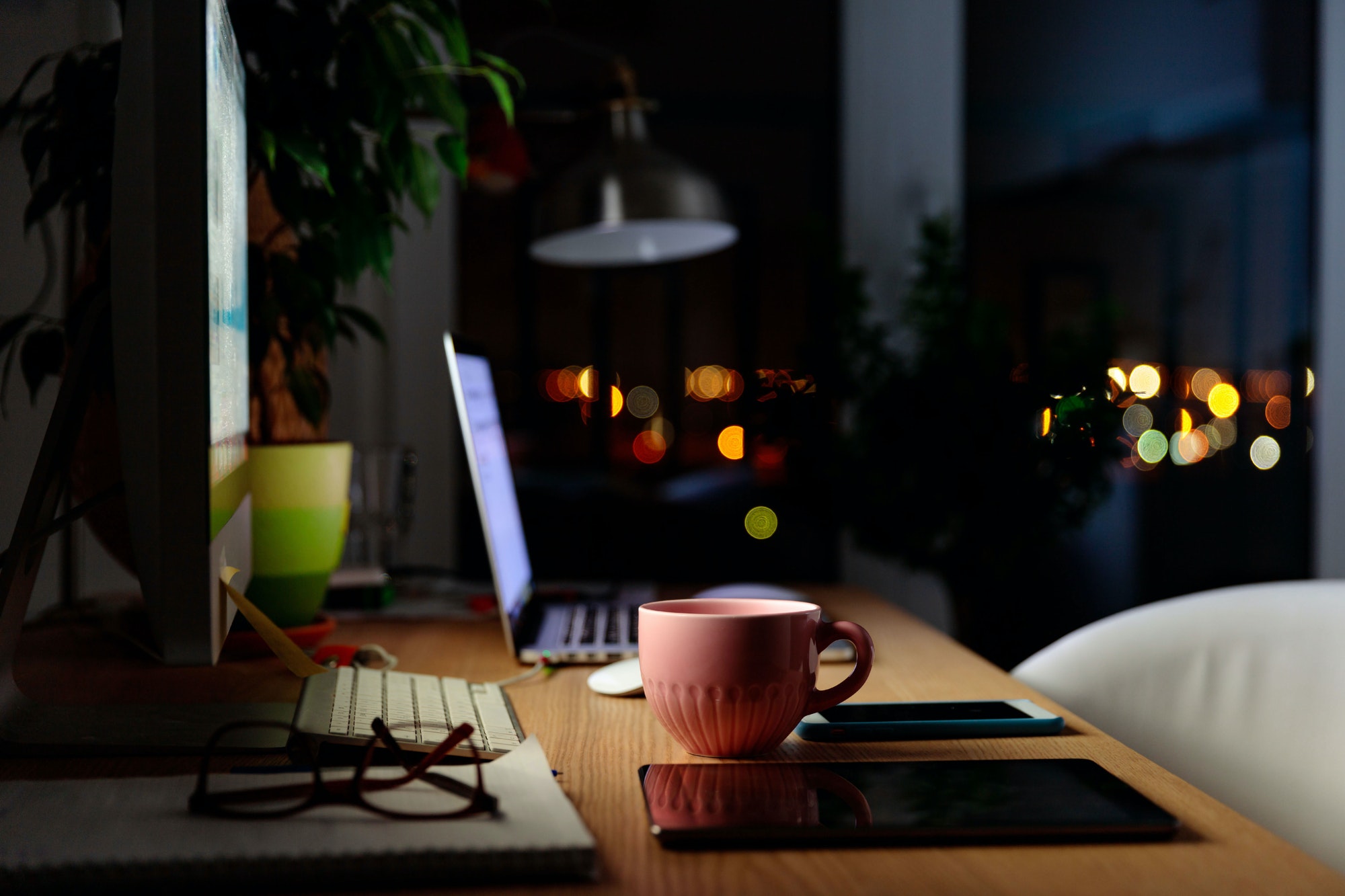 Comfortable workspace for distance job at home - mug of tea, laptop, lamp, tablet, mobile, plant