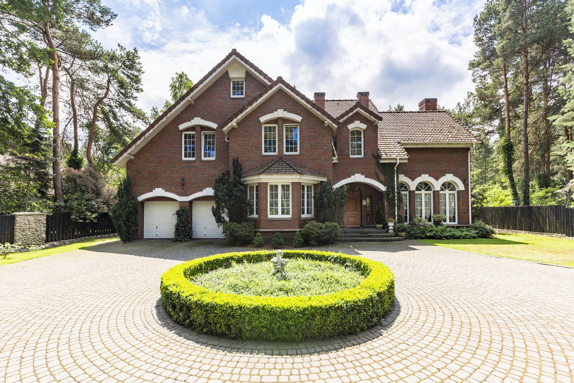 Front view of a driveway with a round garden and big, english st