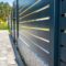 Modern panel fencing in anthracite color, visible spans and a wicket, forest in the background.
