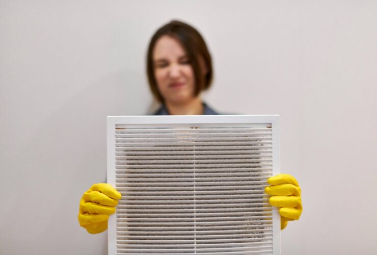Woman holding dirty and dusty ventilation grille, disgusted
