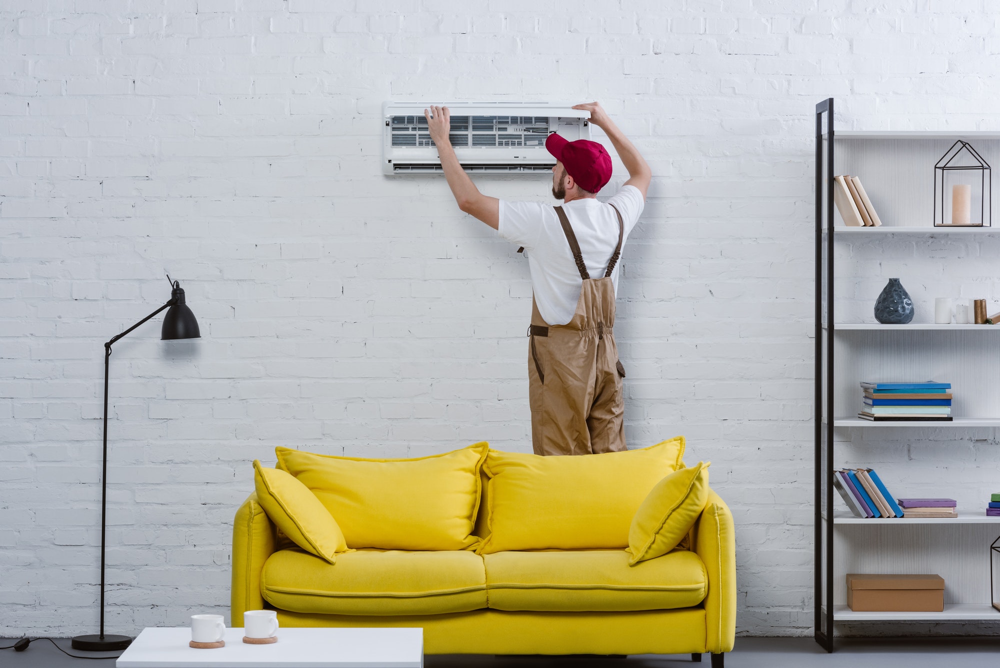 young professional repairman fixing air conditioner hanging on white brick wall