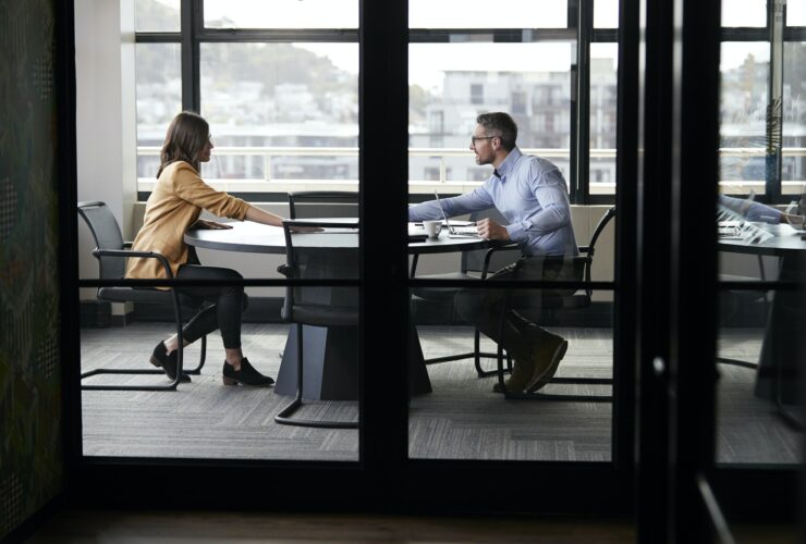 A businessman and young woman meeting for a job interview, full length, seen through glass wall