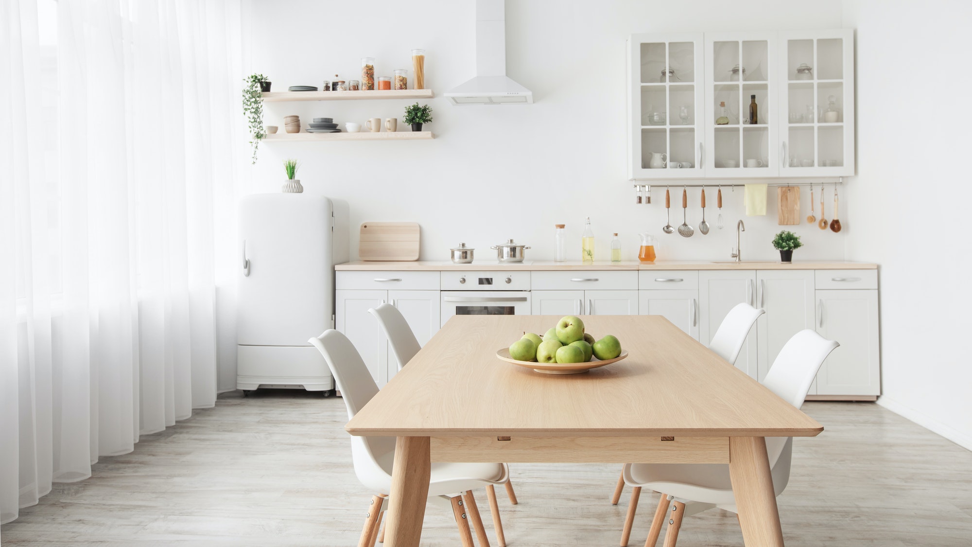 Contemporary minimalist interior of kitchen and dining room. White furniture with utensils and
