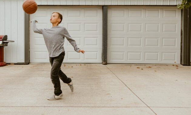 Young boy playing on his driveway at home. Hitting a ball.