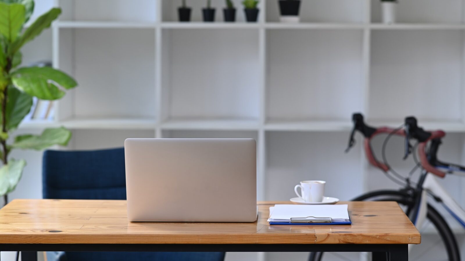 Mock up computer laptop on wooden table with bicycle in home office.