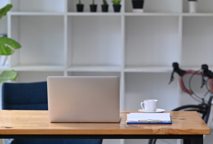 Mock up computer laptop on wooden table with bicycle in home office.