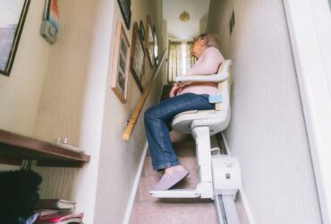 Senior woman using automatic stairlift on a staircase at her home. Medical Stairlift for disabled