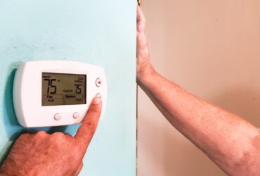 Homeowner adjusting thermostat on hvac using hands while wife watches and complains.