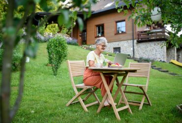 Happy senior woman with laptop working outdoors in garden, home office concept