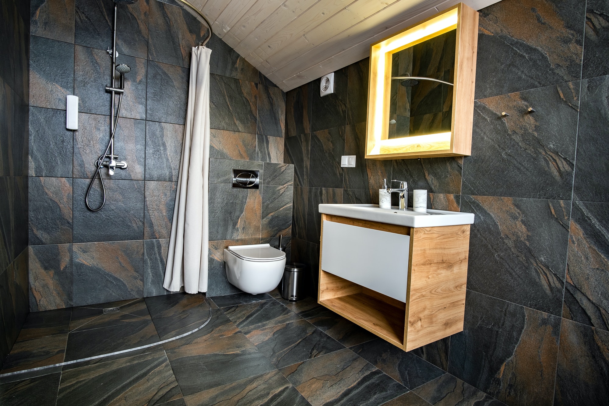 Interior of modern stylish bathroom with black tiled walls, curtain shower place and wooden