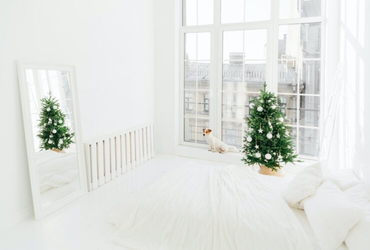 Spacious white bedroom with bed, decorated Christmas tree, mirror and dog on windowsill