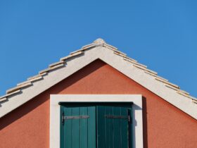 The house on the blue sky background. Roof and window with shutters.