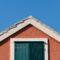 The house on the blue sky background. Roof and window with shutters.