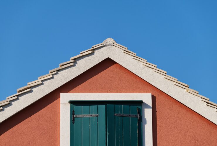 The house on the blue sky background. Roof and window with shutters.