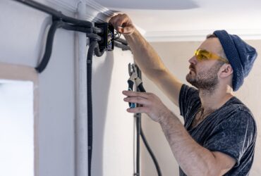 An electrician is mounting electric sockets on the white wall indoors.