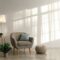 Comfortable retro armchair with pillow, luminous lamp and plant in pot, ottoman on floor