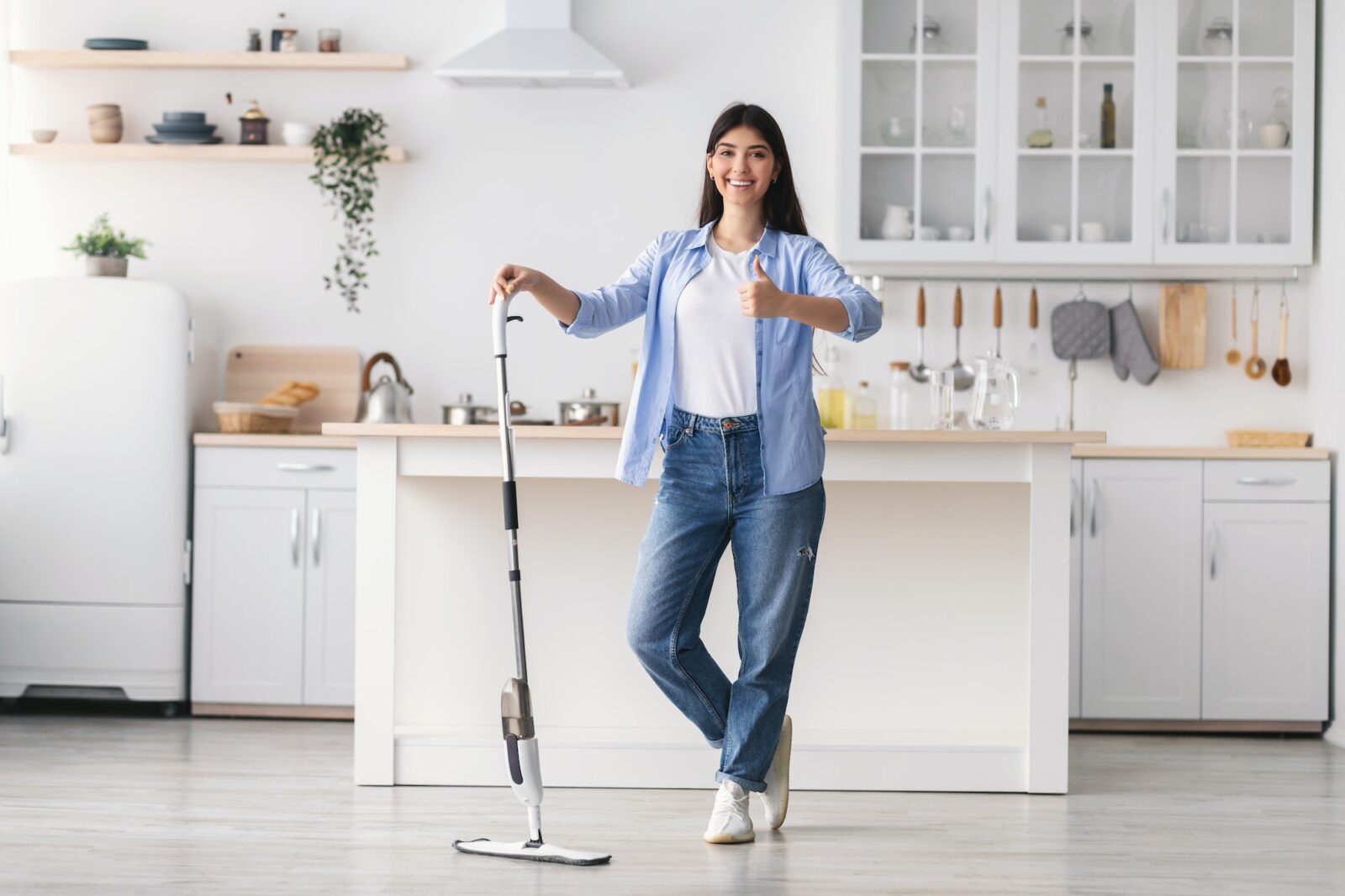 Happy woman showing thumbs up cleaning floor with spray mop