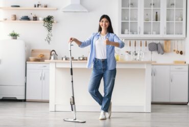 Happy woman showing thumbs up cleaning floor with spray mop