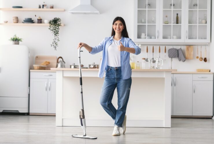 Happy woman showing thumbs up cleaning floor with spray mop
