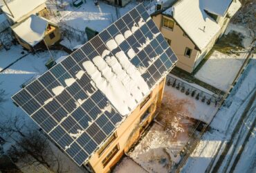 House roof covered with solar panels in winter with snow on top. Energy efficiency and maintenance