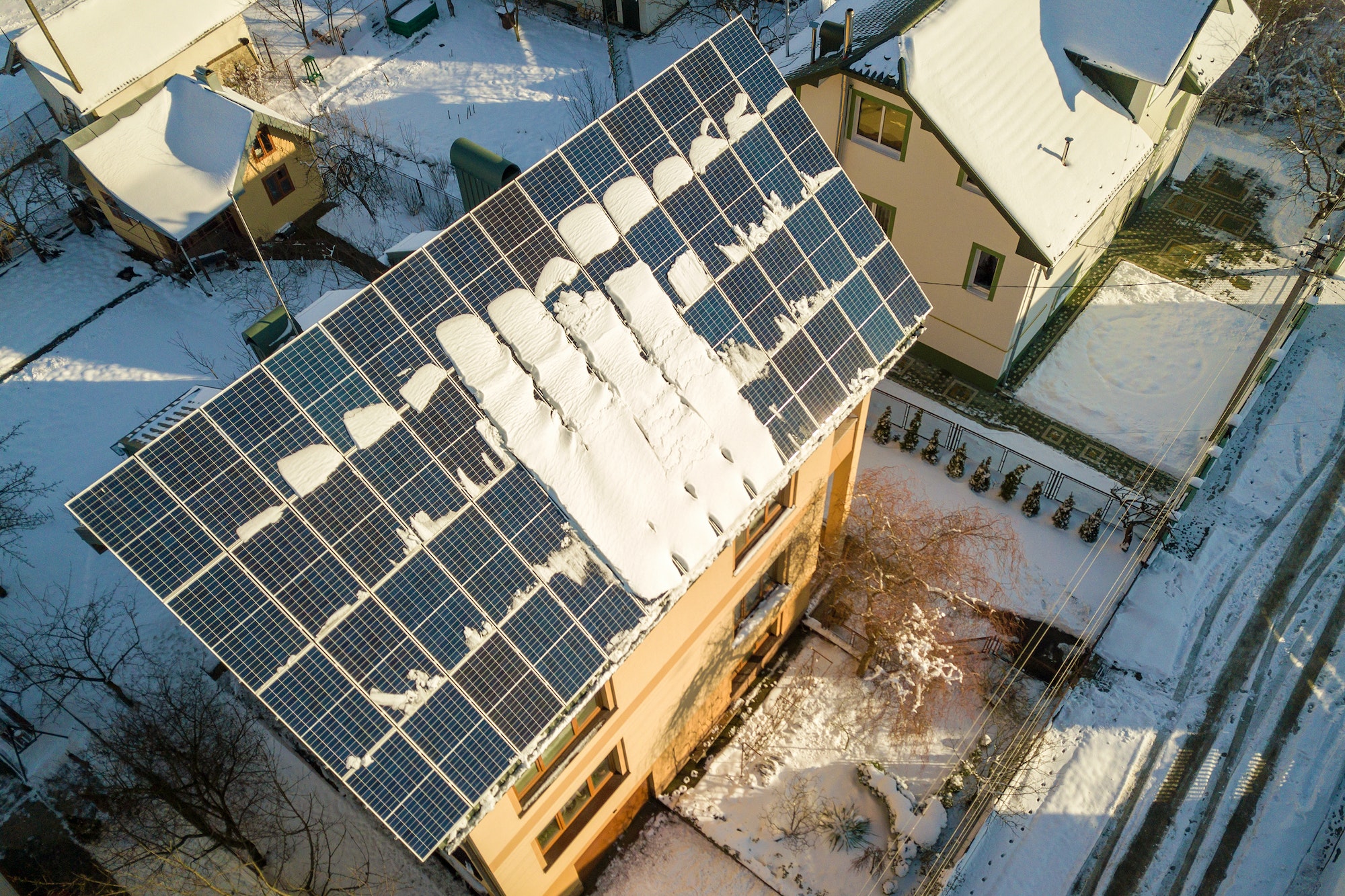 House roof covered with solar panels in winter with snow on top. Energy efficiency and maintenance