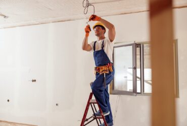 Smiling electrician fixing electric cable on ceiling