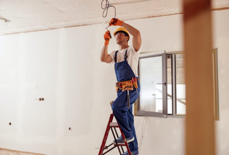 Smiling electrician fixing electric cable on ceiling