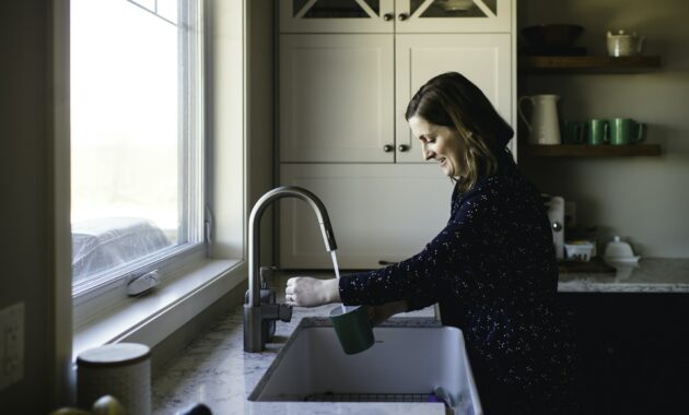 Woman filling up cup at kitchen sink