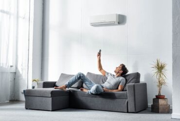 handsome man lying on sofa and switching on air conditioner