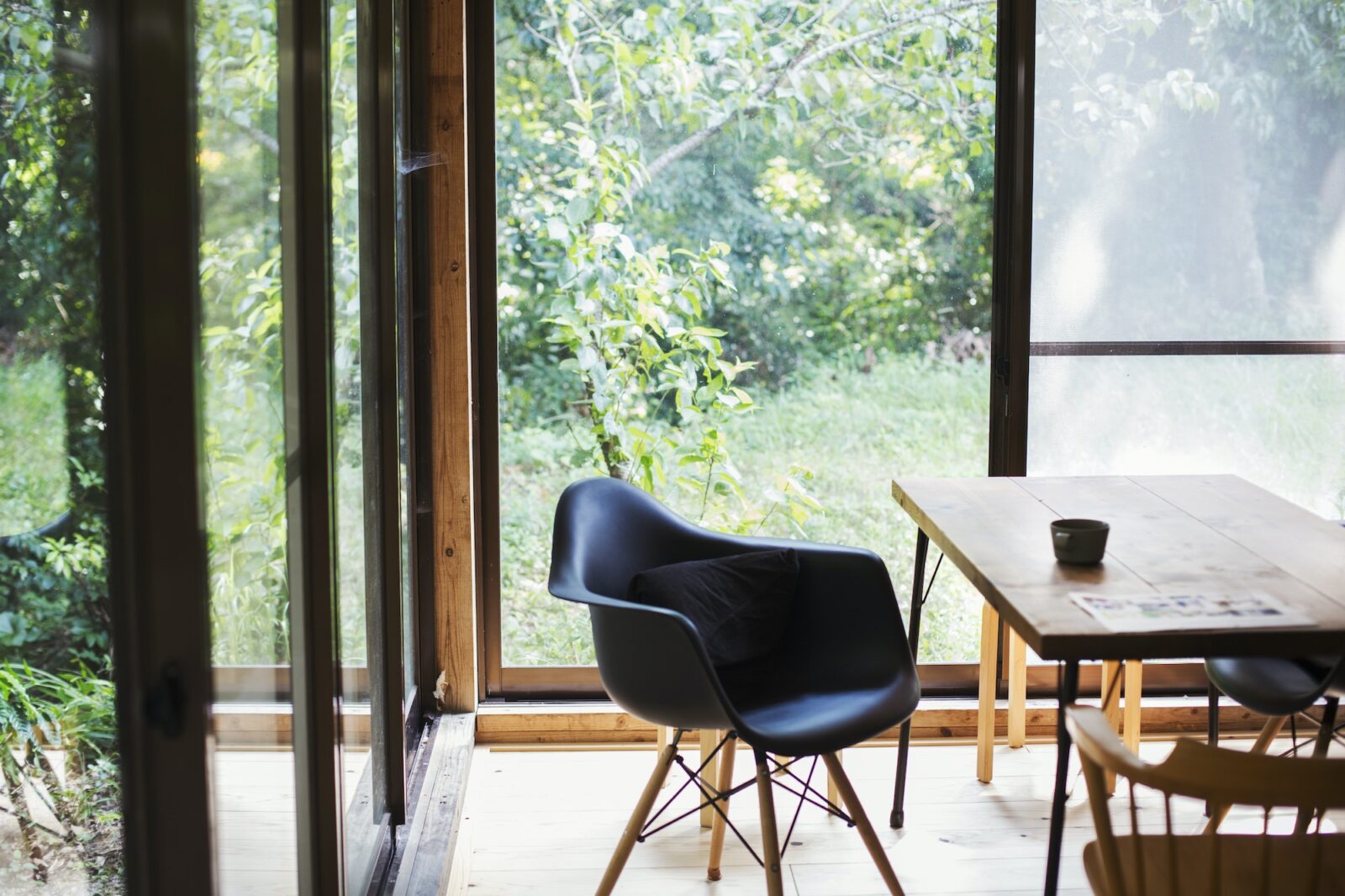 Interior view of residential building with black chair and wooden table, glass walls.