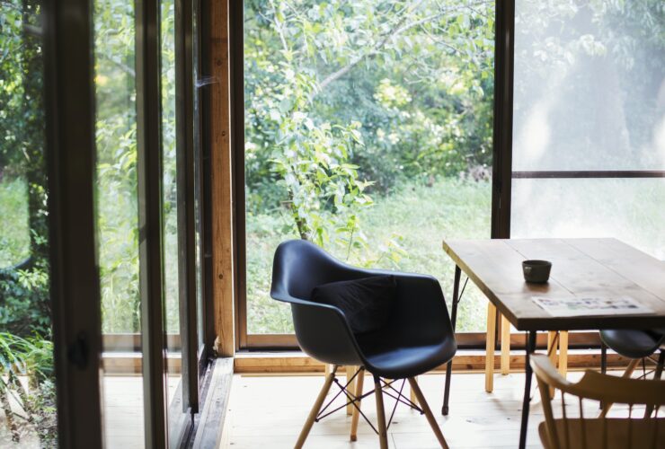 Interior view of residential building with black chair and wooden table, glass walls.
