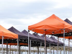 Many foldable canopy tents with light bulbs decoration for outdoors event against cloudy sky