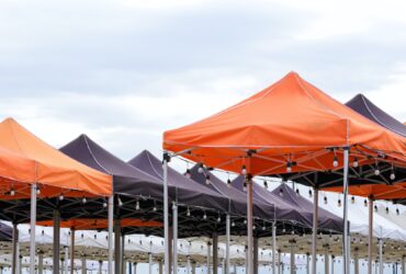 Many foldable canopy tents with light bulbs decoration for outdoors event against cloudy sky