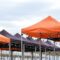 Many foldable canopy tents with light bulbs decoration for outdoors event against cloudy sky