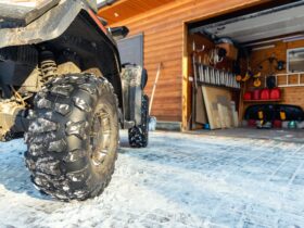 Back POVview of quad bike offroad vehicle parked front house garage door on snowy cold winter day.