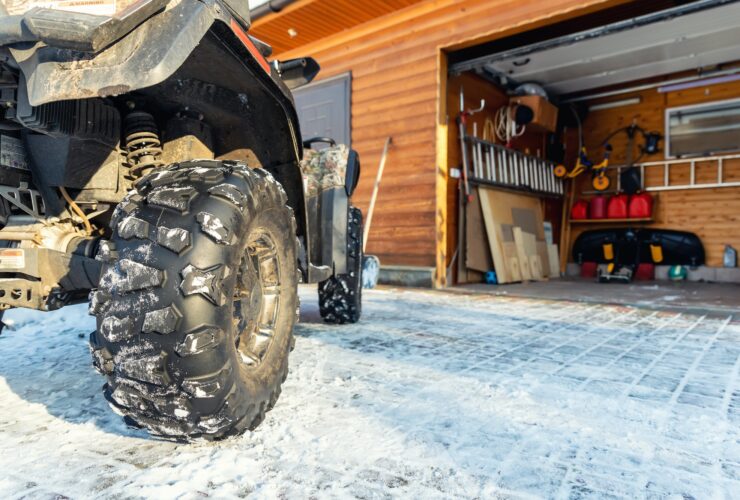 Back POVview of quad bike offroad vehicle parked front house garage door on snowy cold winter day.