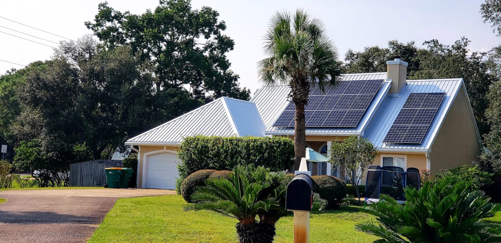 Beach house with solar panels on rooftop for energy surrounded by palm trees for tropical vibes.