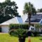 Beach house with solar panels on rooftop for energy surrounded by palm trees for tropical vibes.