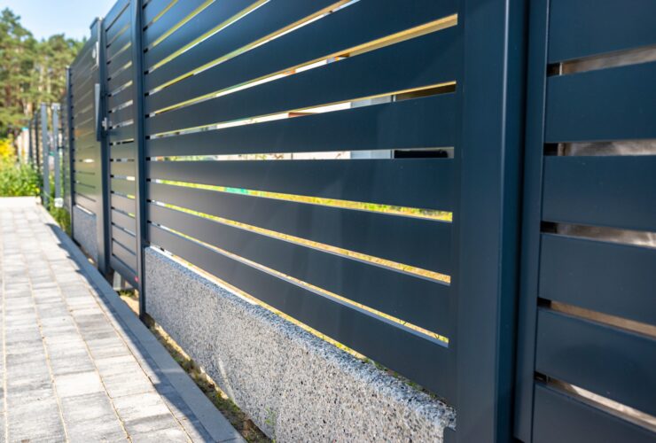 Modern panel fencing in anthracite color, visible spans and a wicket, forest in the background.
