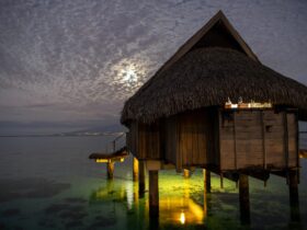 Overwater bungalow hut seen at night under cloudy sky on tropical island