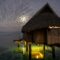 Overwater bungalow hut seen at night under cloudy sky on tropical island