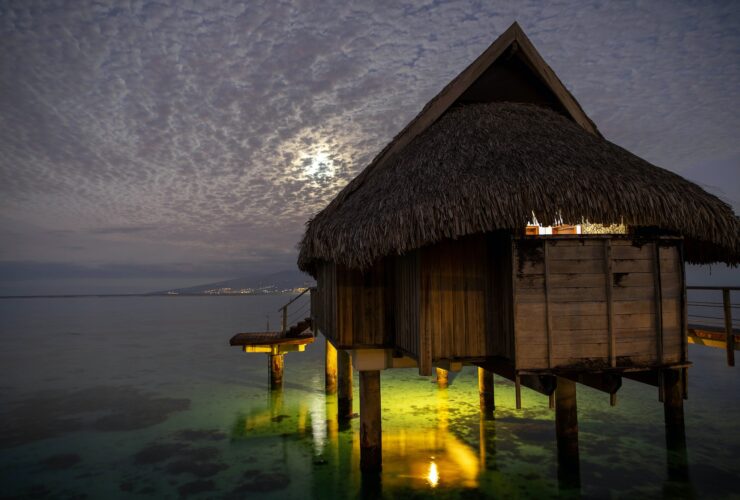 Overwater bungalow hut seen at night under cloudy sky on tropical island
