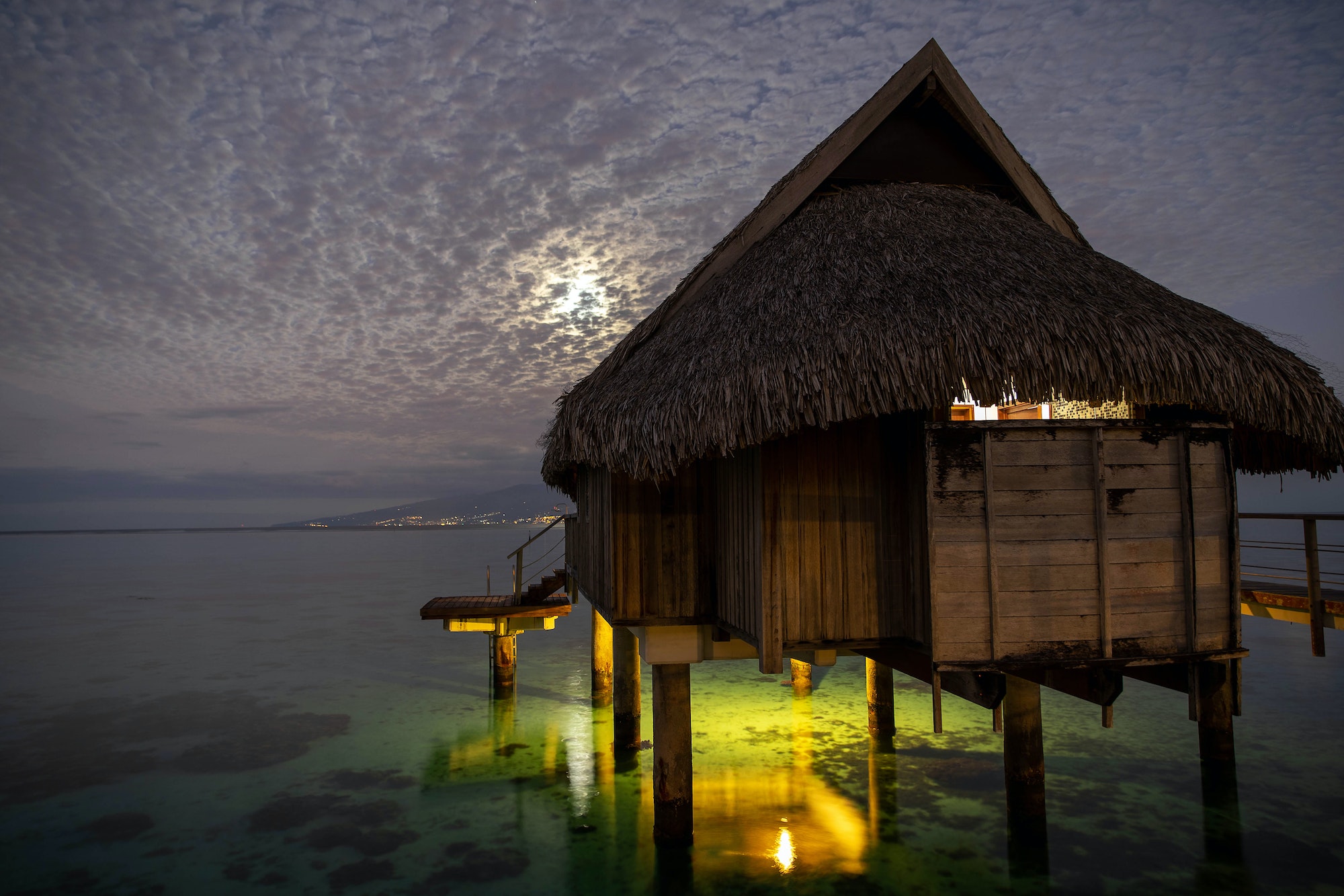 Overwater bungalow hut seen at night under cloudy sky on tropical island