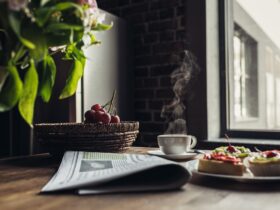 Still life of newspaper, breakfast with cakes and hot coffee on kitchen table in front of window