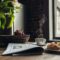 Still life of newspaper, breakfast with cakes and hot coffee on kitchen table in front of window