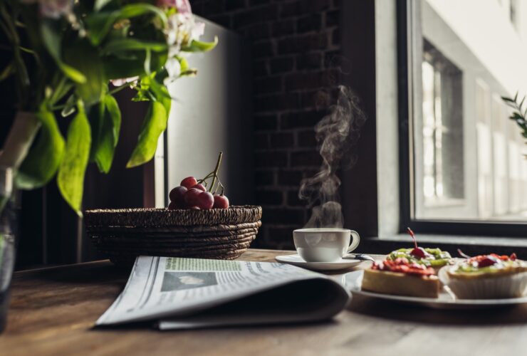 Still life of newspaper, breakfast with cakes and hot coffee on kitchen table in front of window