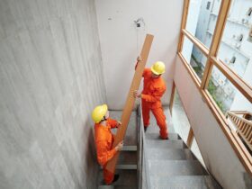 Workers Carrying Board up Narrow Stairs