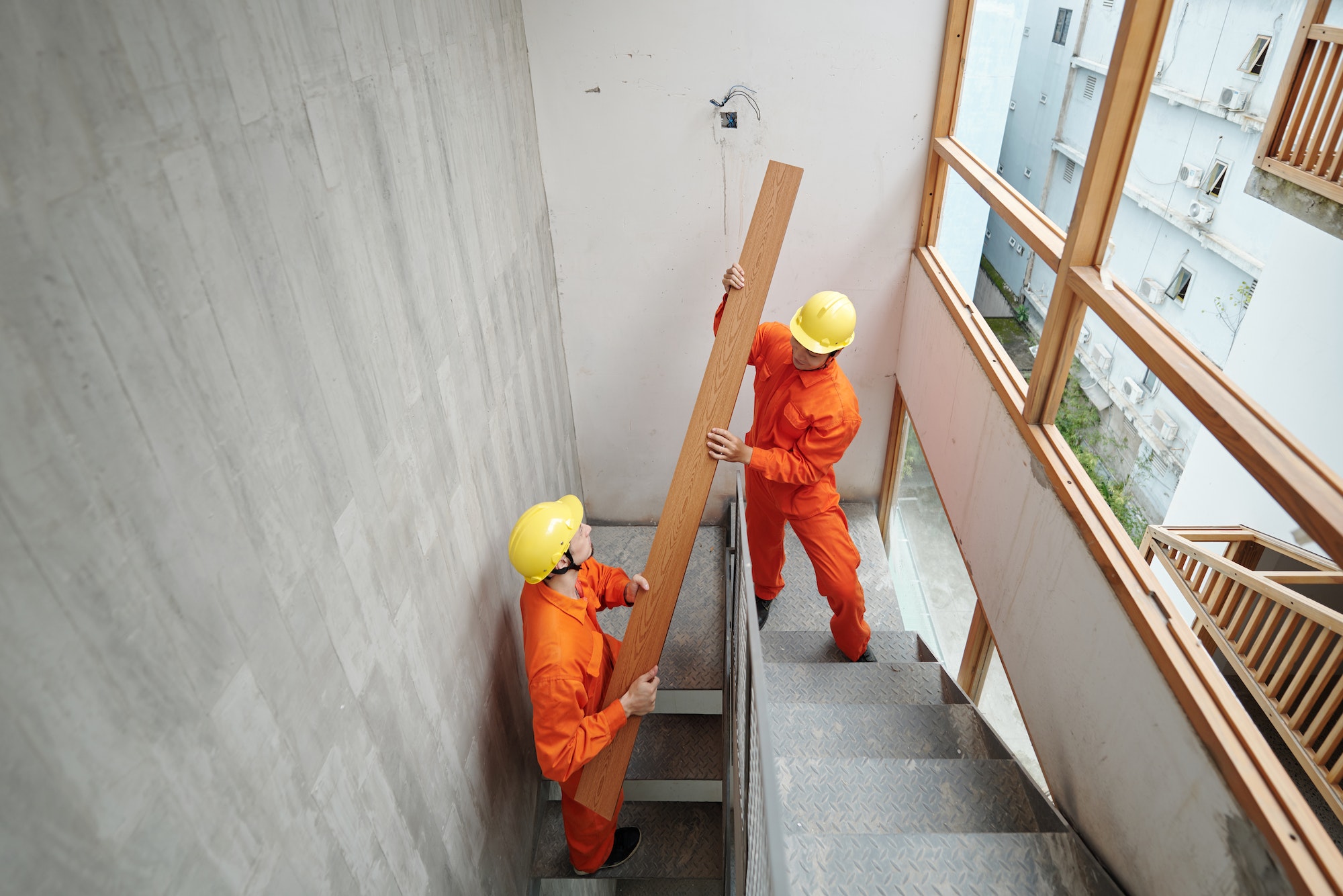 Workers Carrying Board up Narrow Stairs