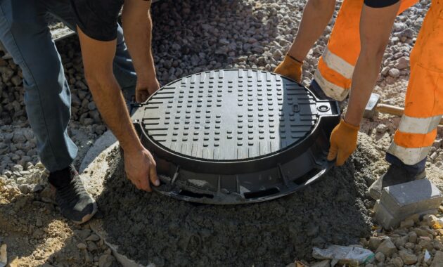 A worker installs a sewer manhole on a septic tank made of concrete rings